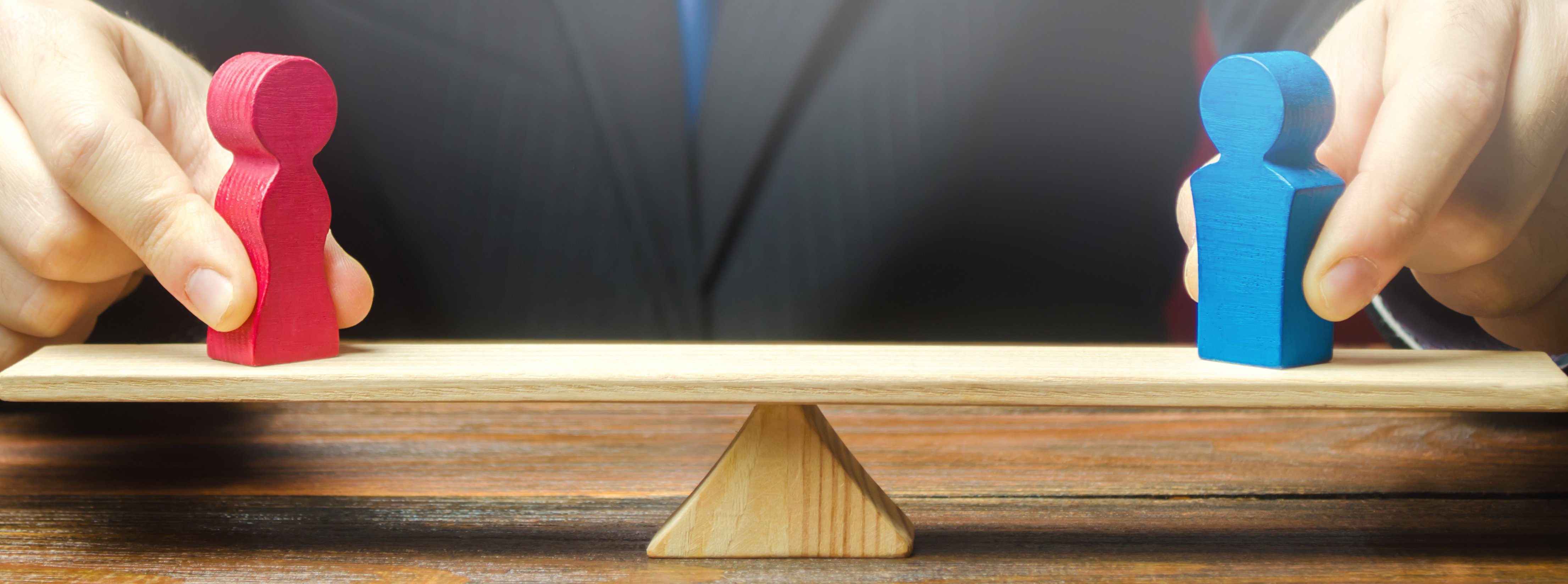 Image: Man balancing red and blue wooden figures on a seesaw, symbolizing the shared responsibility of cloud providers in cybersecurity.